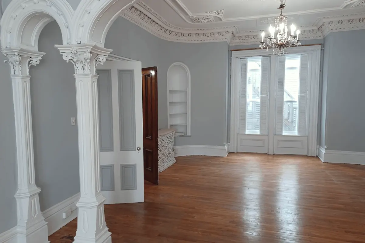 A restored room: white columns and arches, a plaster ceiling with a chandelier, and wood floors.